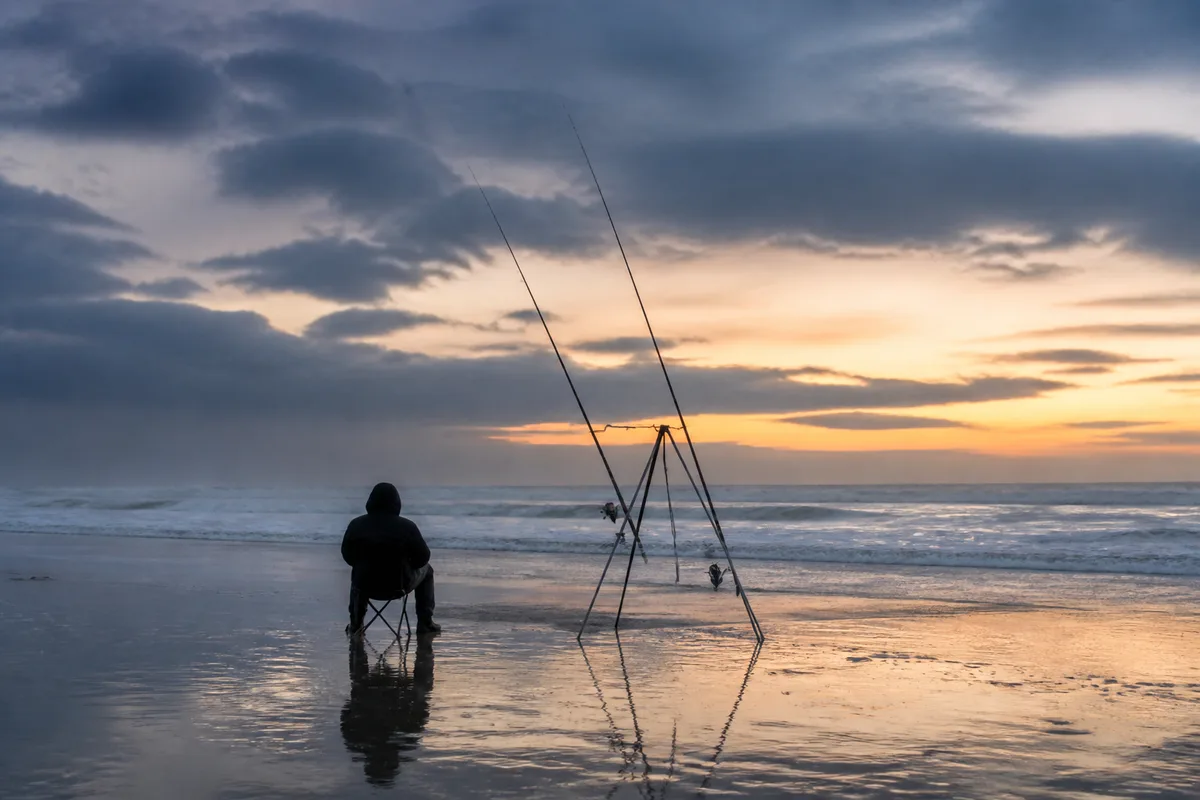 Pêcheur installé sur une plage des Landes au crépuscule avec deux cannes de surfcasting sur trépied